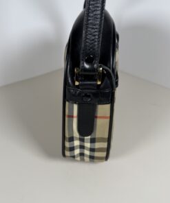 Side profile of Burberrys crossbody bag showing black leather strap attachment and gold-tone hardware.