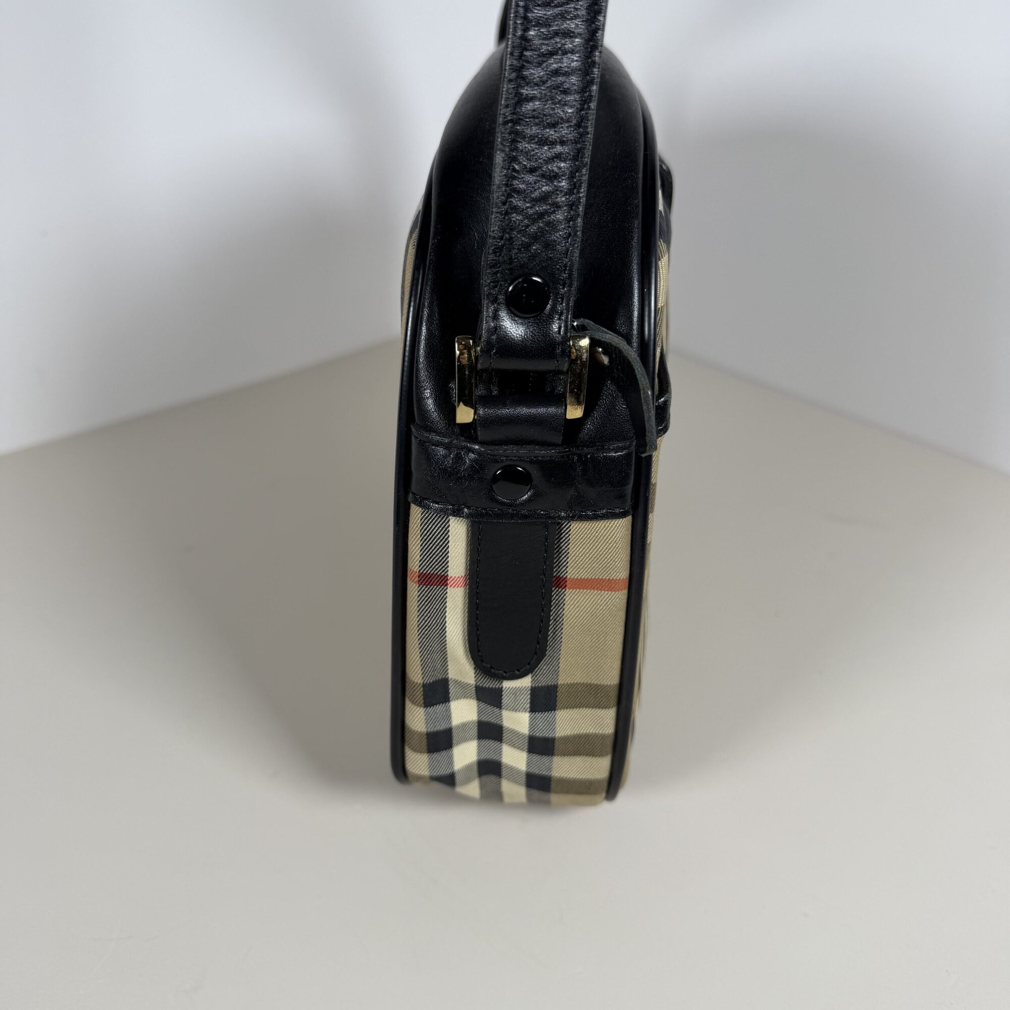 Side profile of Burberrys crossbody bag showing black leather strap attachment and gold-tone hardware.