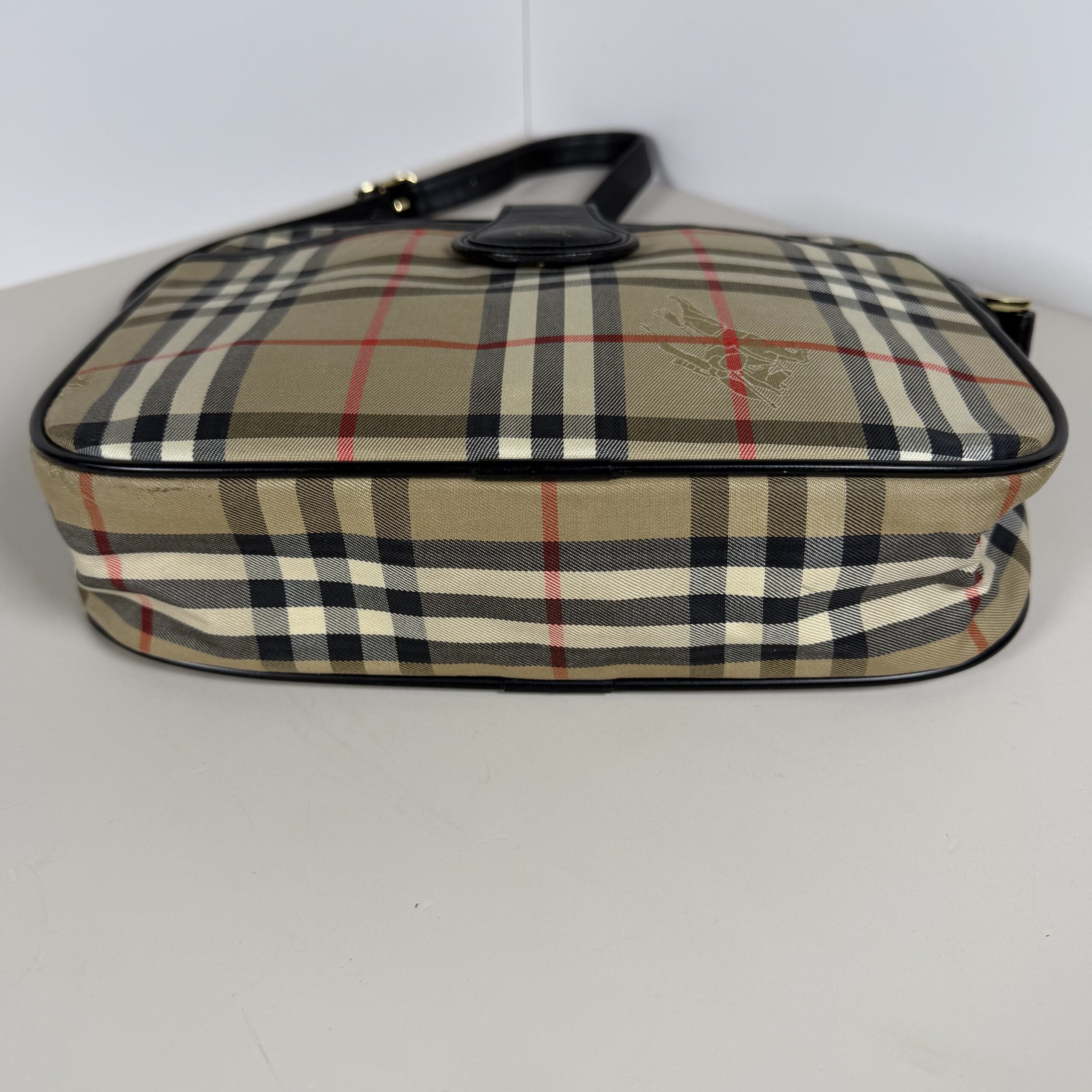 Bottom base of Burberrys Haymarket check crossbody bag framed with black leather piping.