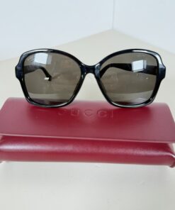 Front view of black Gucci oversized sunglasses resting on a red Gucci case.
