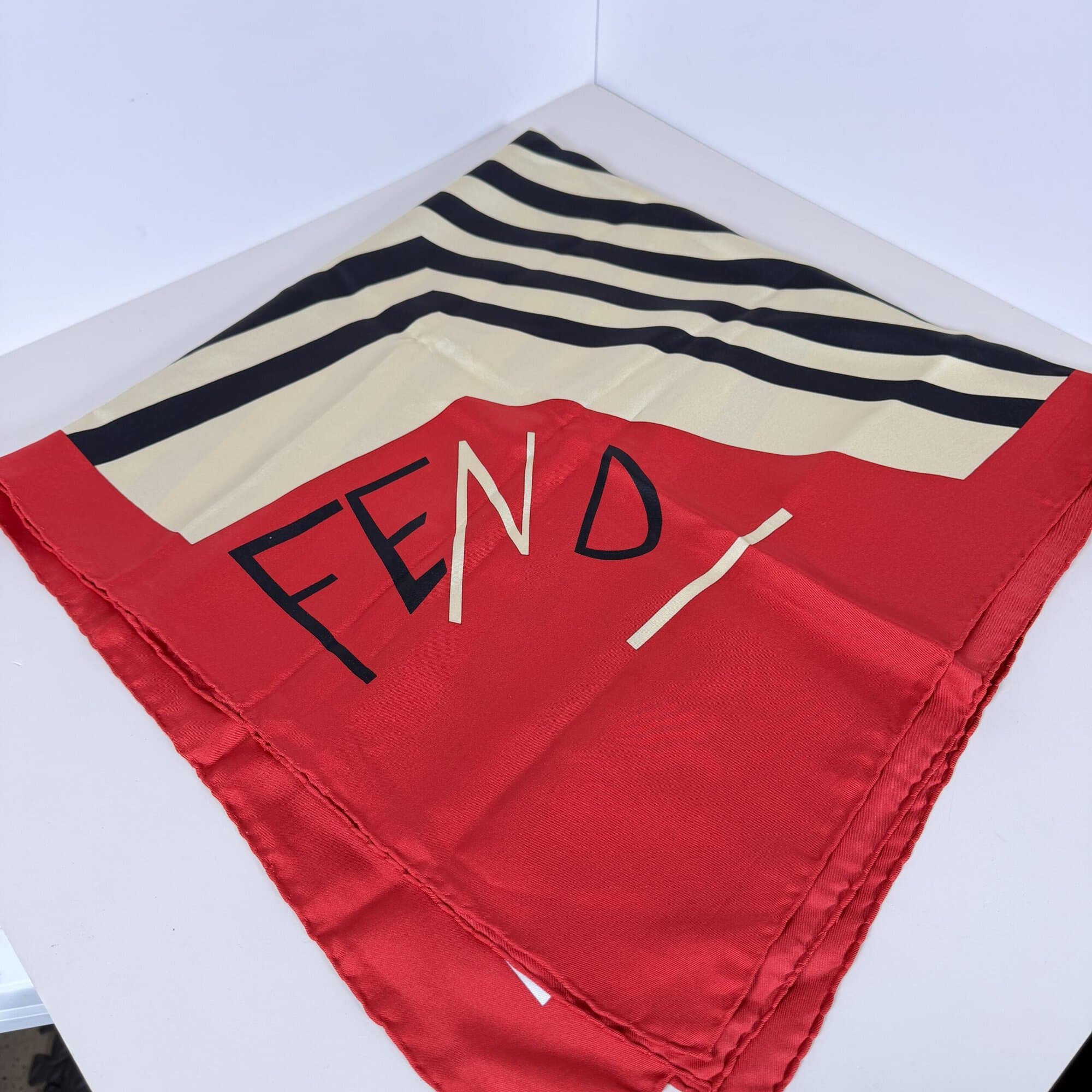 Fendi silk foulard scarf folded showing red corner with stylized script logo and black chevron stripes.