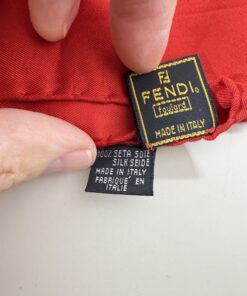 Close-up of hand holding Fendi foulard label and composition tag reading Made in Italy.