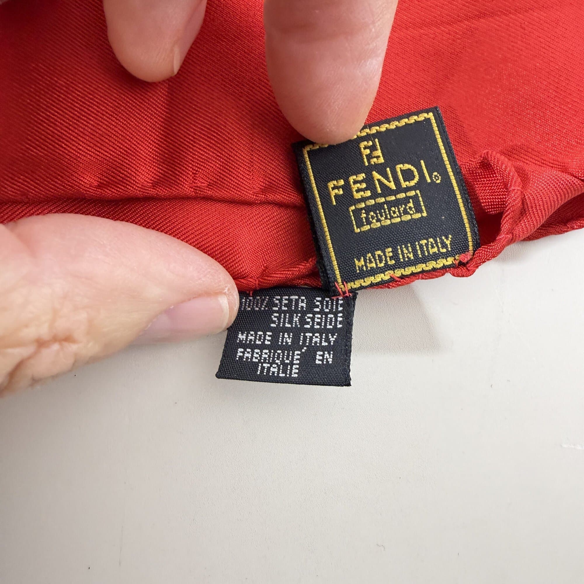 Close-up of hand holding Fendi foulard label and composition tag reading Made in Italy.