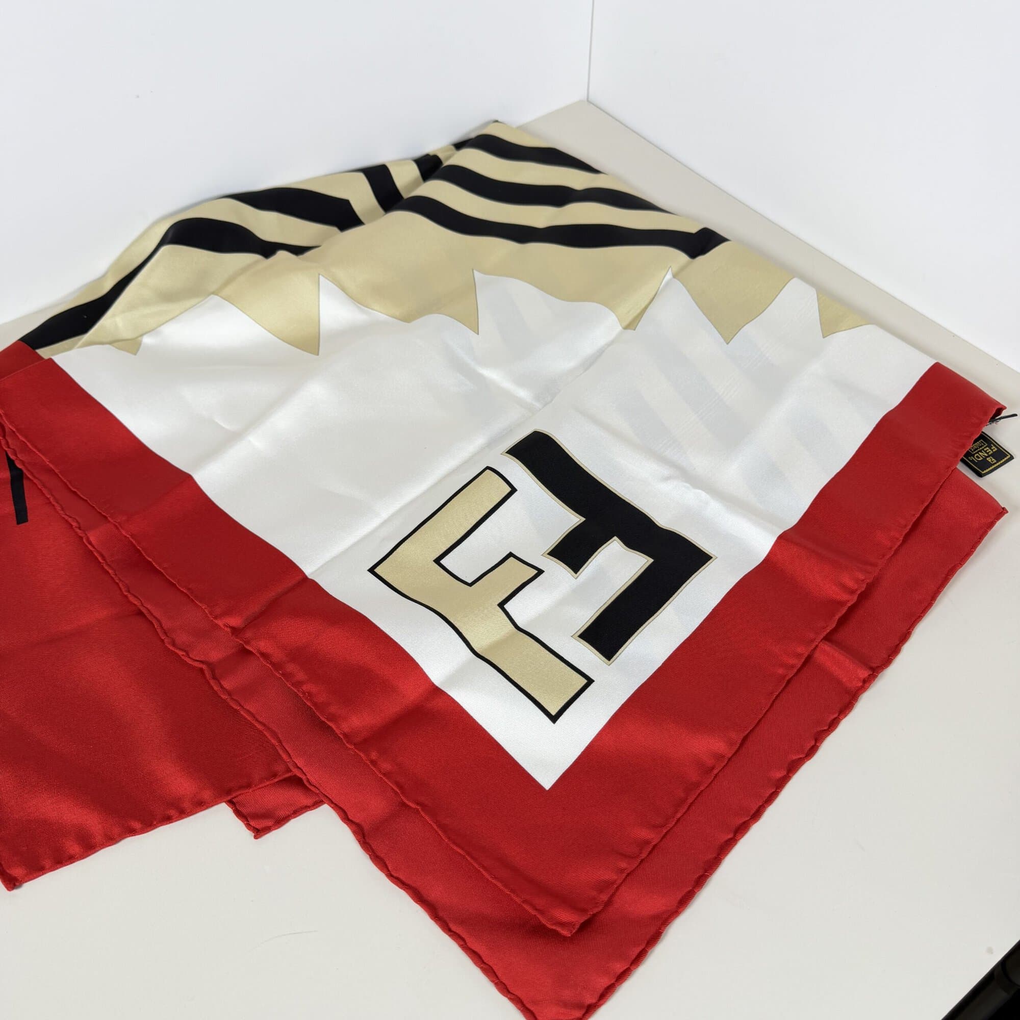 Folded Fendi silk scarf displaying bold FF block logo corner with red border and chevron pattern.