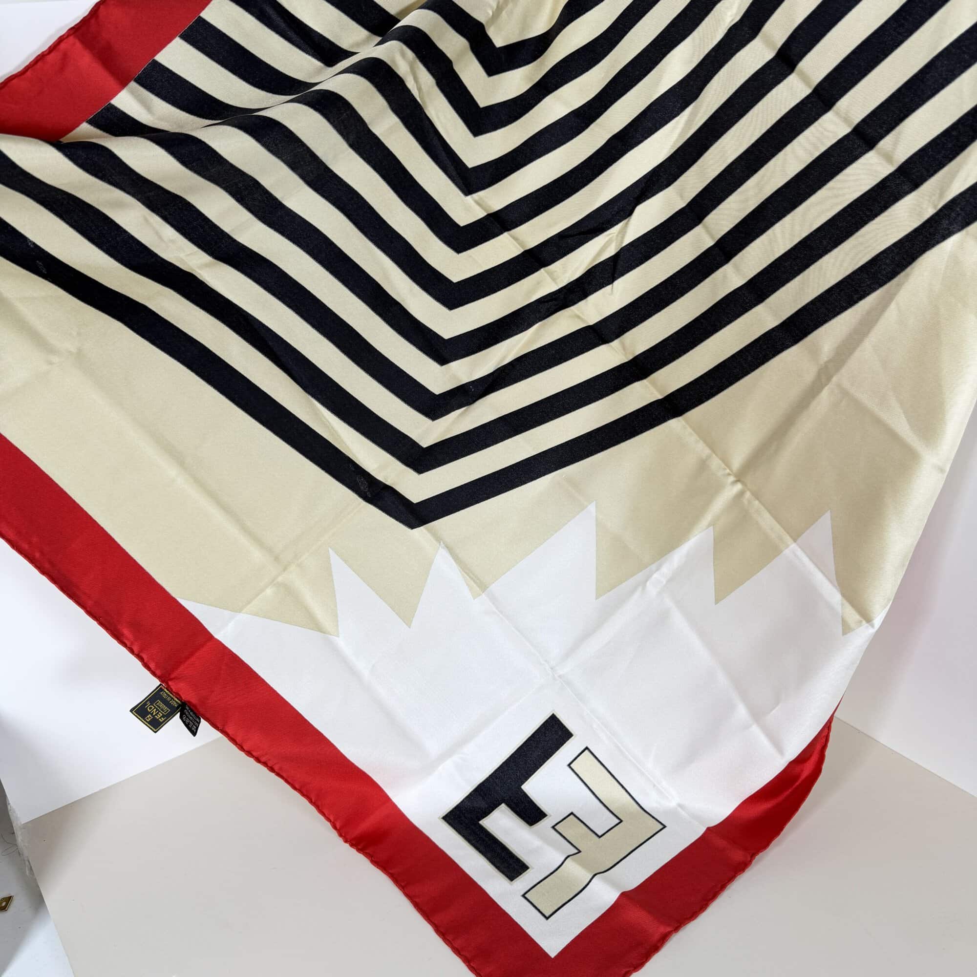 Overhead view of Fendi silk scarf spread open showing black and cream chevron center and red borders.