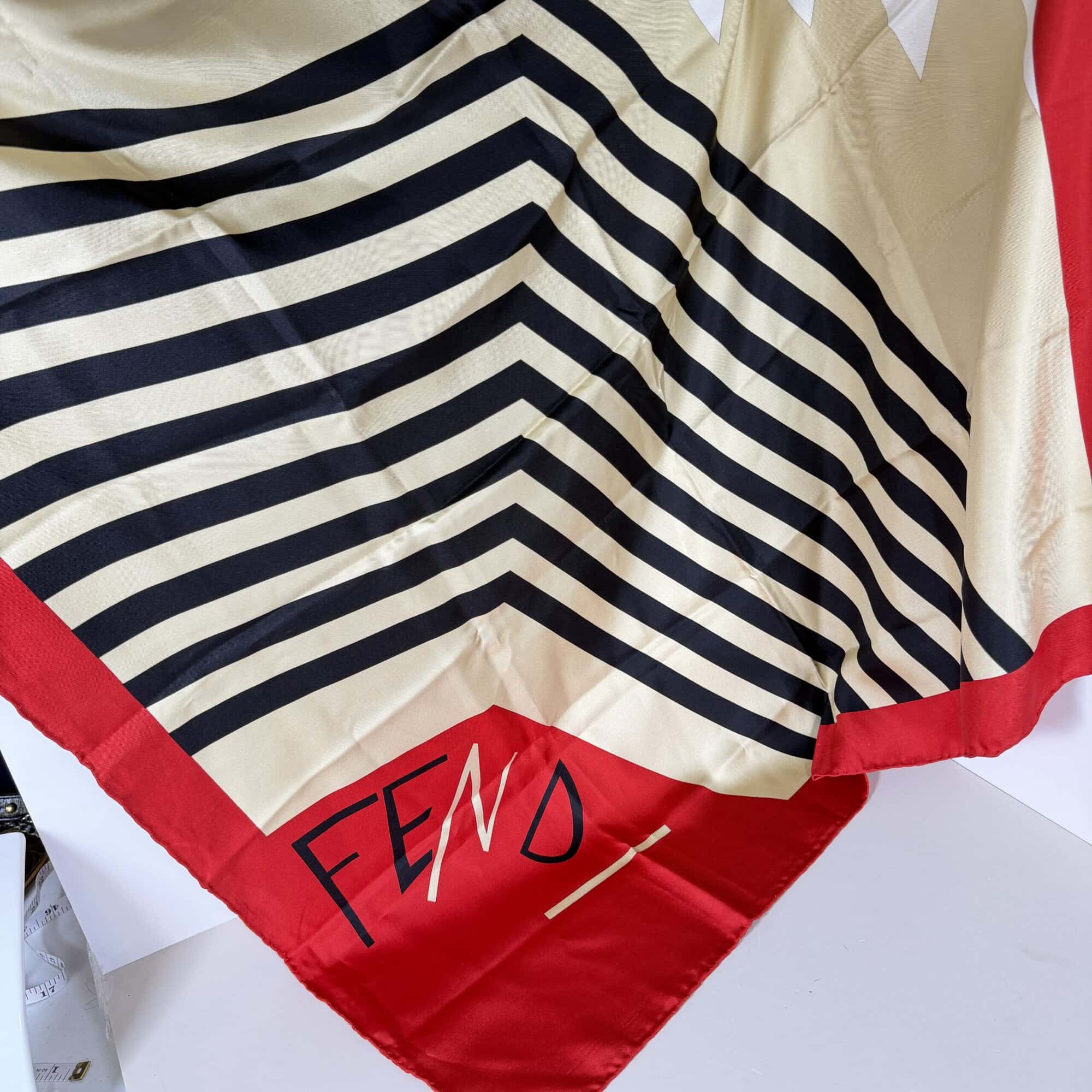 Fendi silk scarf spread showing script logo corner, striped chevron center, and red borders.