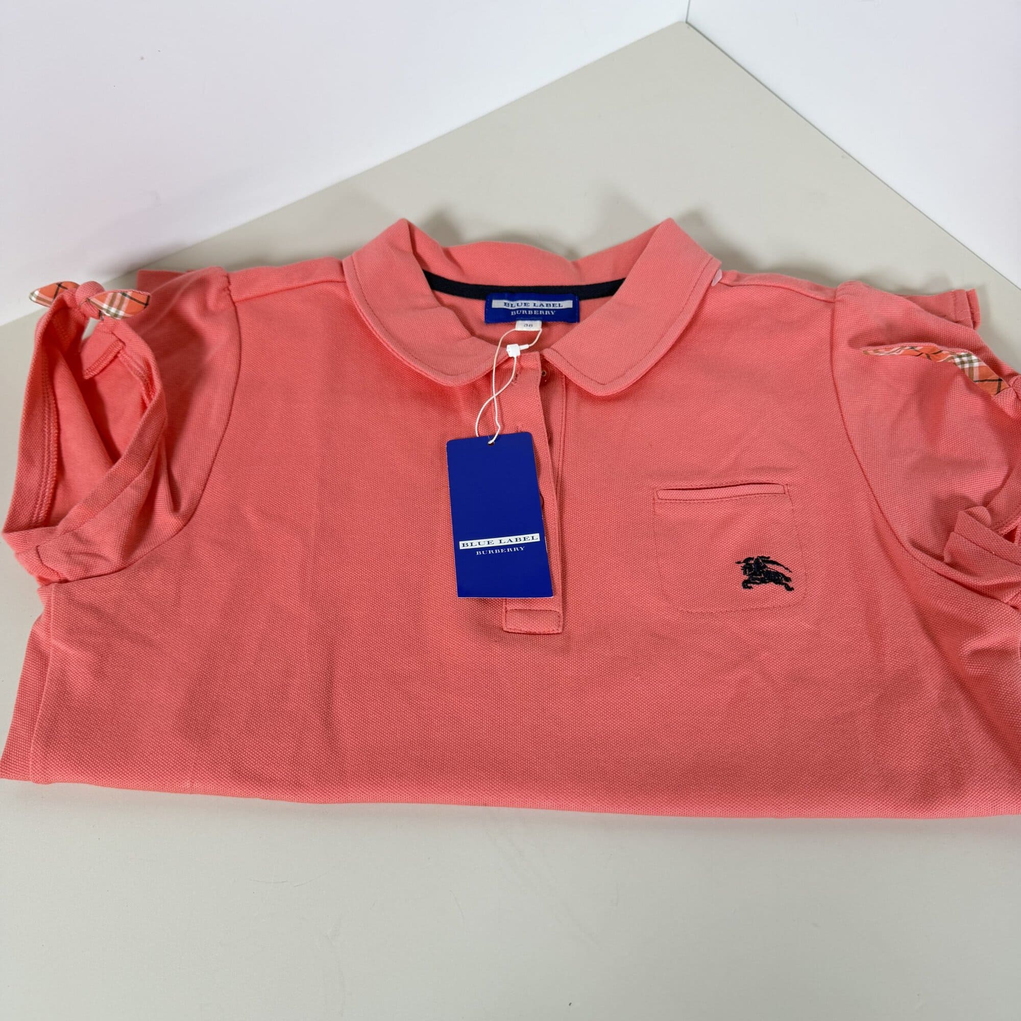 Folded coral Burberry Blue Label polo shirt showing collar, chest logo, and attached tag