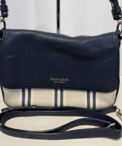 Close-up of Kate Spade navy pebbled leather flap with gold logo over striped canvas body.